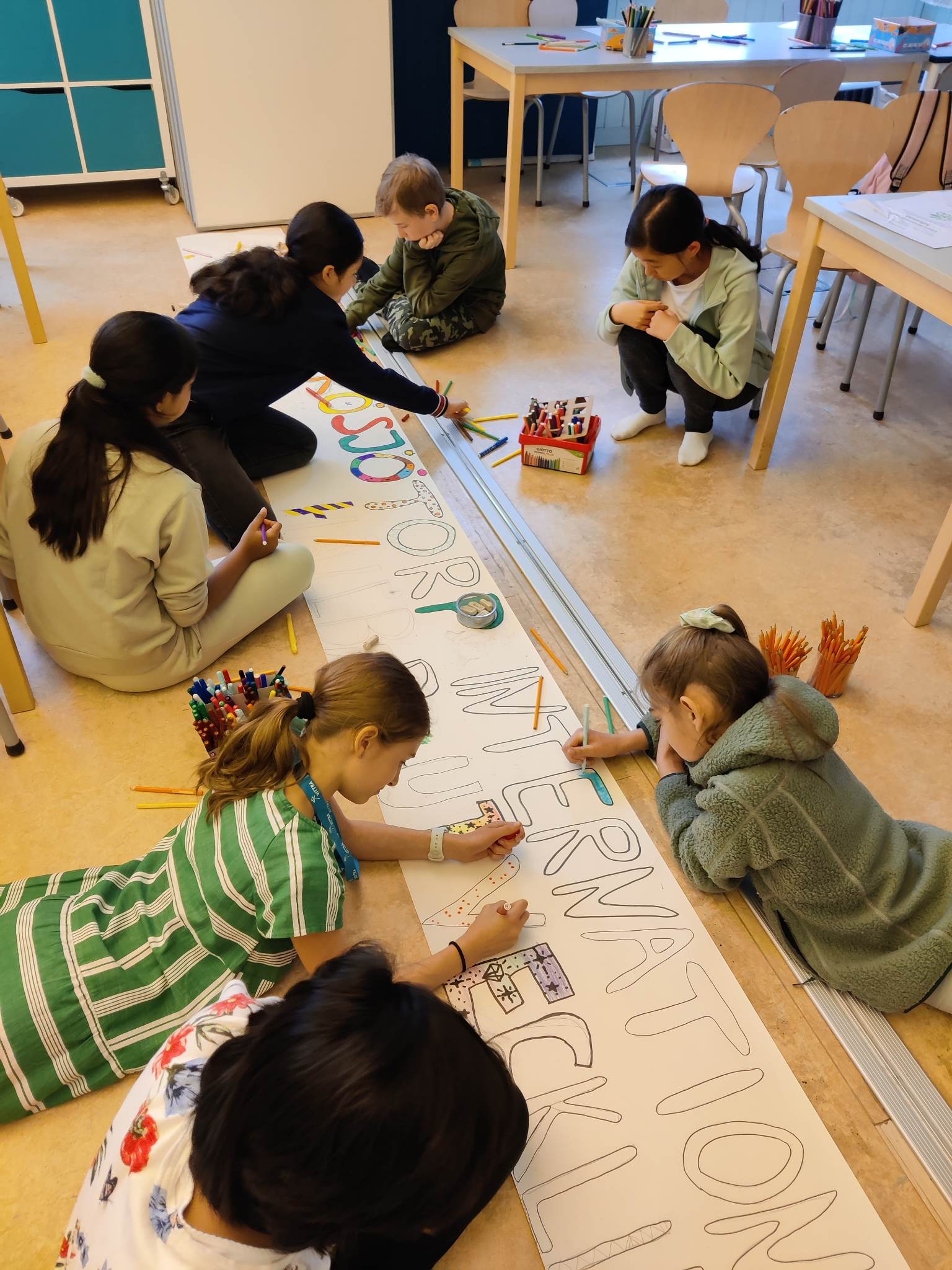 Elever på Vittra Rösjötorp ligger på golvet och gör en skylt