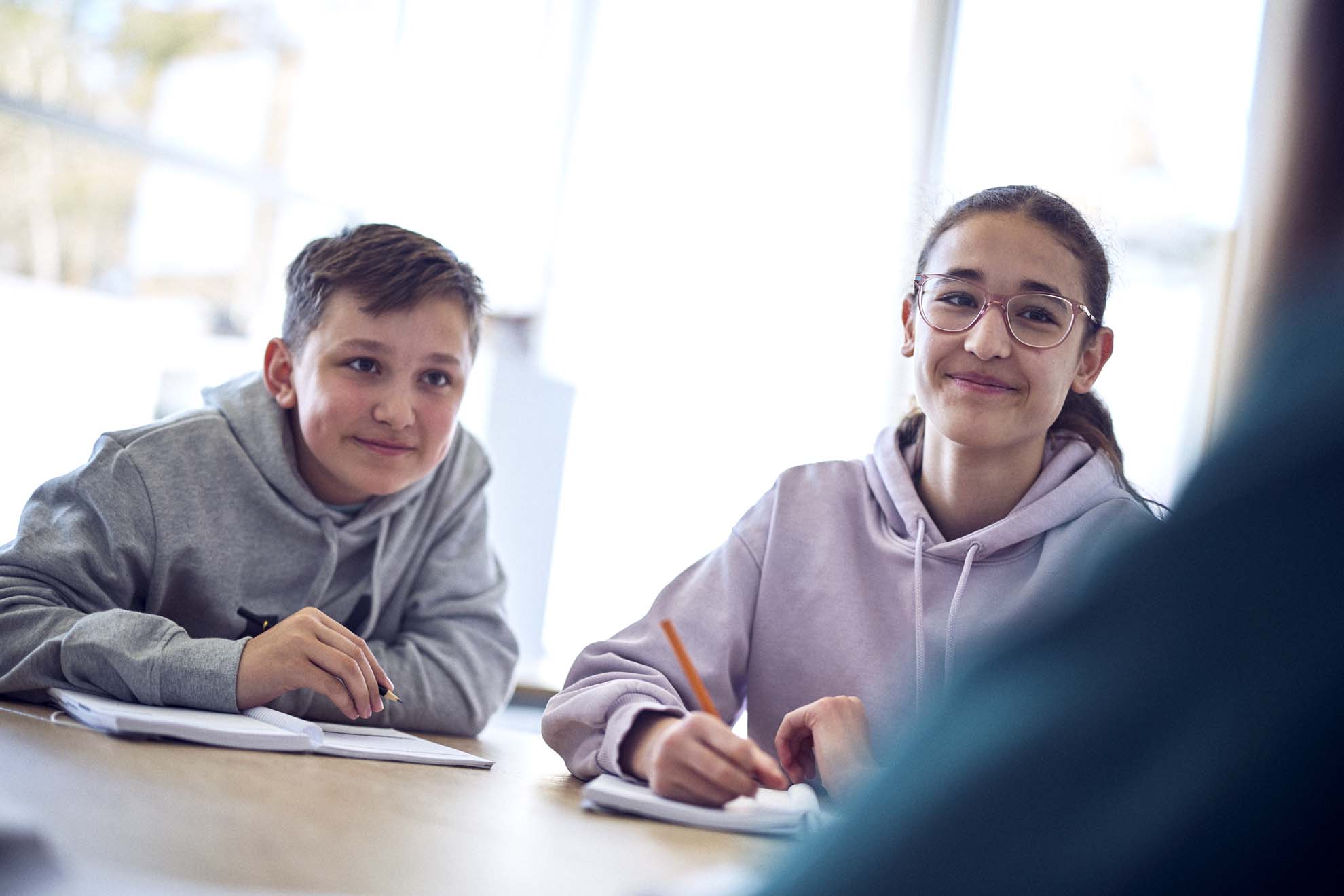 Två elever sitter i sina skolbänkar och skriver