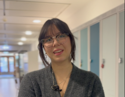 Eleven Amy står framför skåpen på skolan. Hon har på sig glasögon och har brunt hår med lugg.