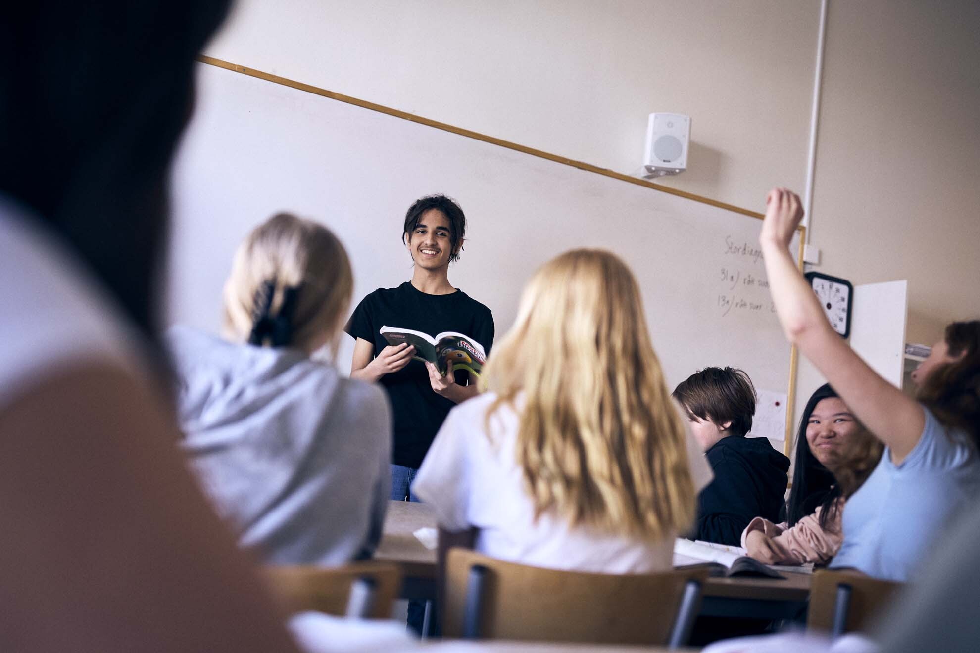 Elever i klassrummet. En elev står framför klassen och de andra lyssnar engagerat.