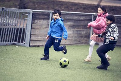 Tre elever på Vittra spelar fotboll utomhus.