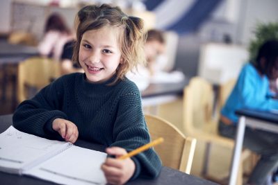 En elev i förskoleklass på Vittra skriver i en bok under en lektion.