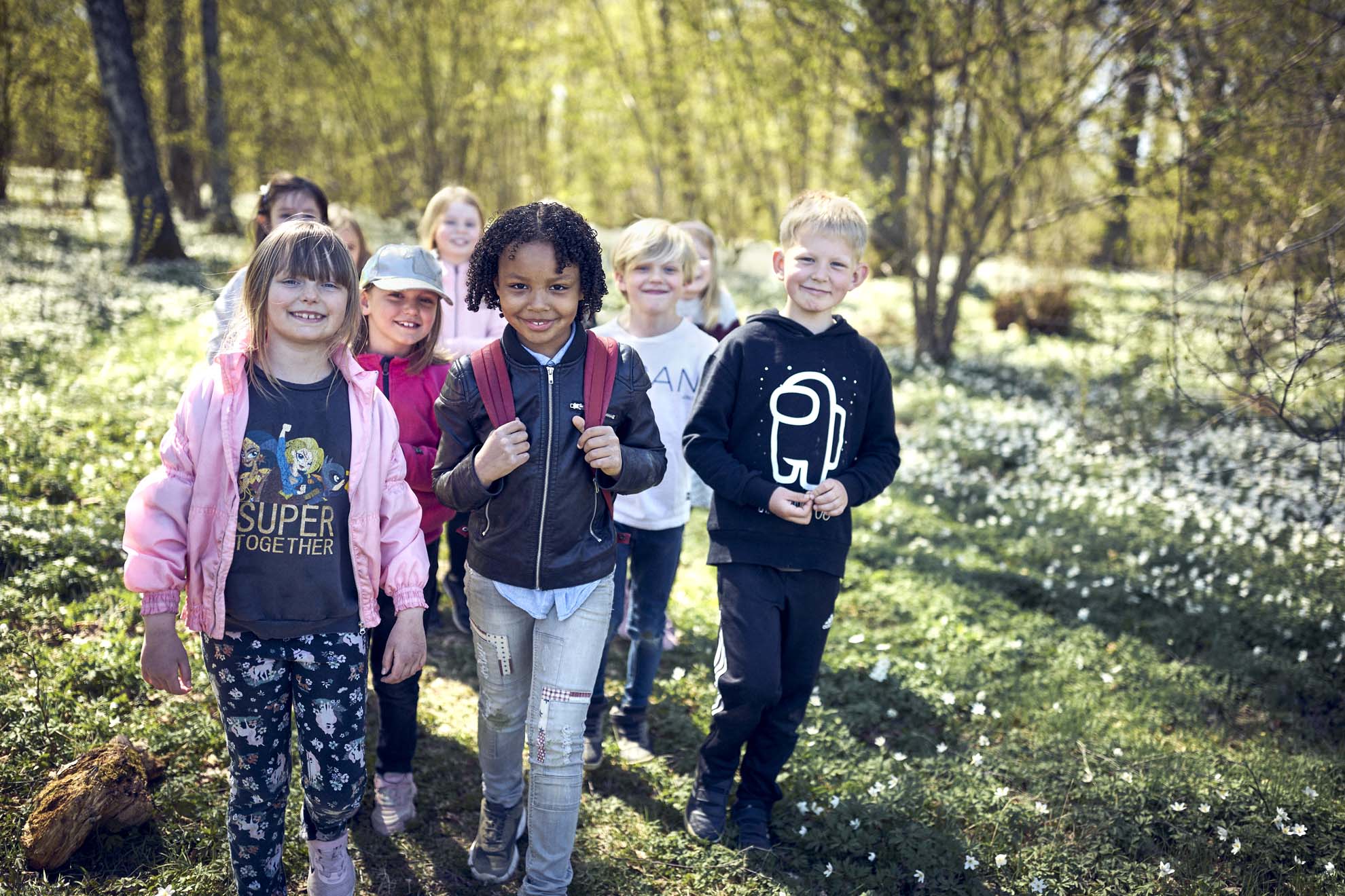 En skolklass går ute i en skog med vitsippor