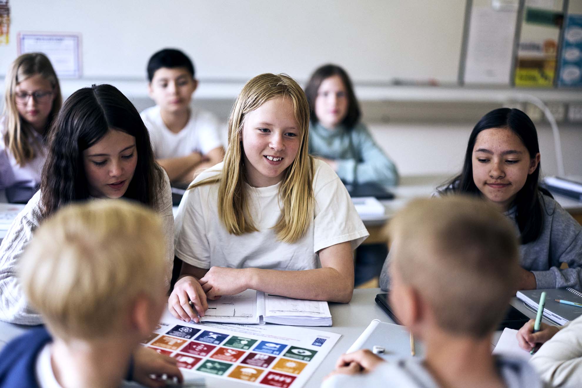 Nio elever sitter vid sina skolbänkar i sitt klassrum och arbetar med FN's globala mål.