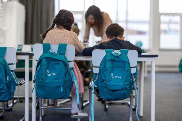 Två elever sitter i ett klassrum, på stolarna hänger blå Vittra-ryggsäckar.