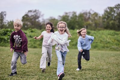 Fyra elever springer ute på gräset och ler mot kameran