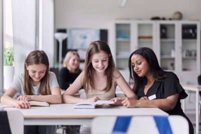 Två elever läser och en pedagog sitter brevid och hjälper till.