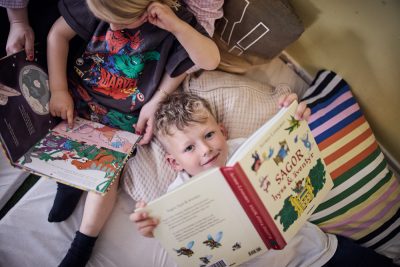 Pojke ligger i läshörna och läser bok men kollar upp i kameran.