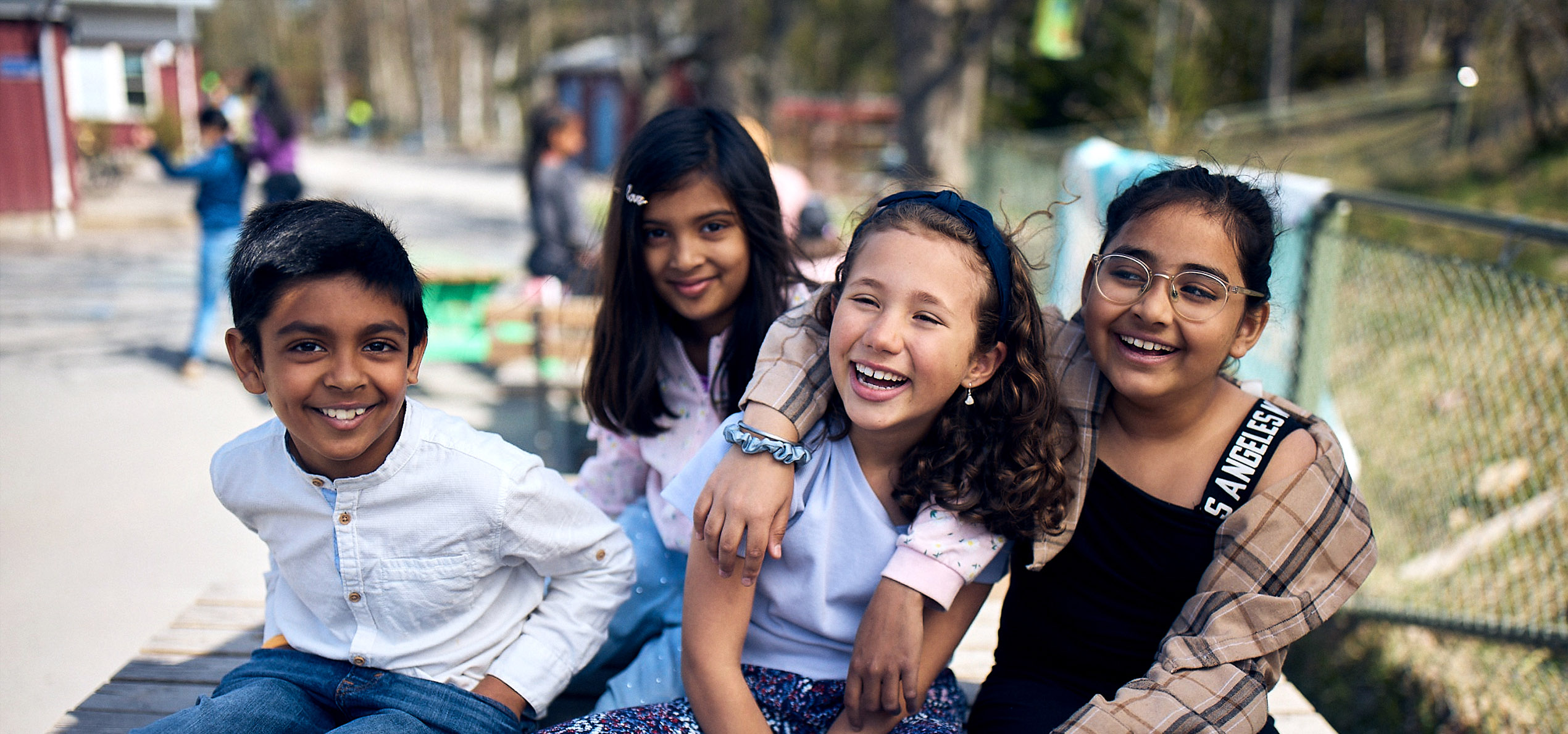 Fyra glada elever sitter på en bänk på skolgården på Vittra.