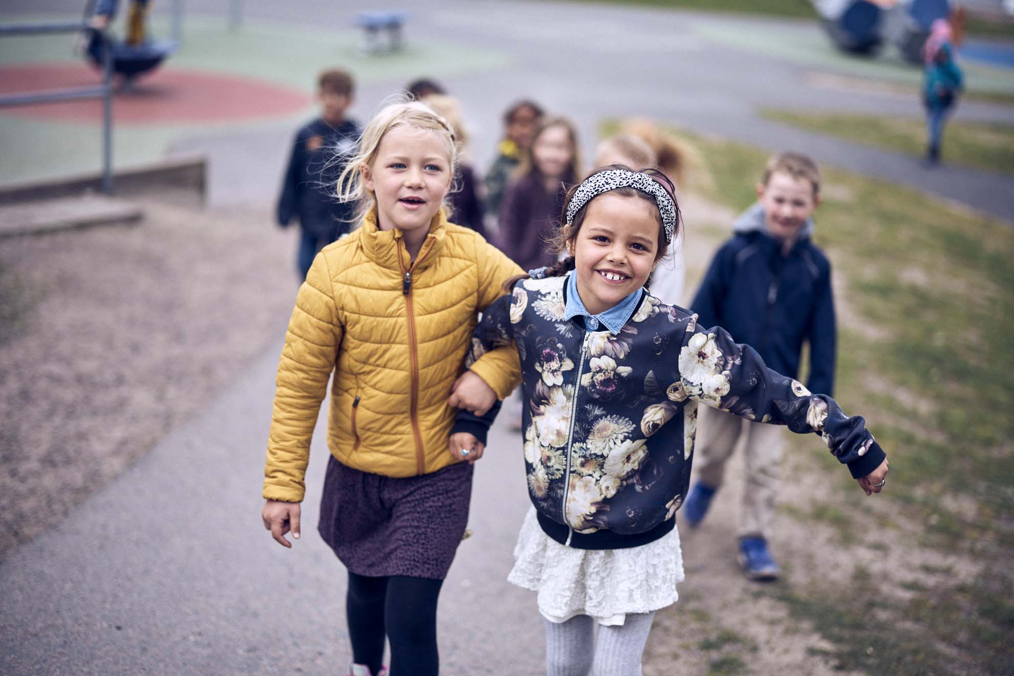 Två glada elever håller armkrok och går ute på skolgården