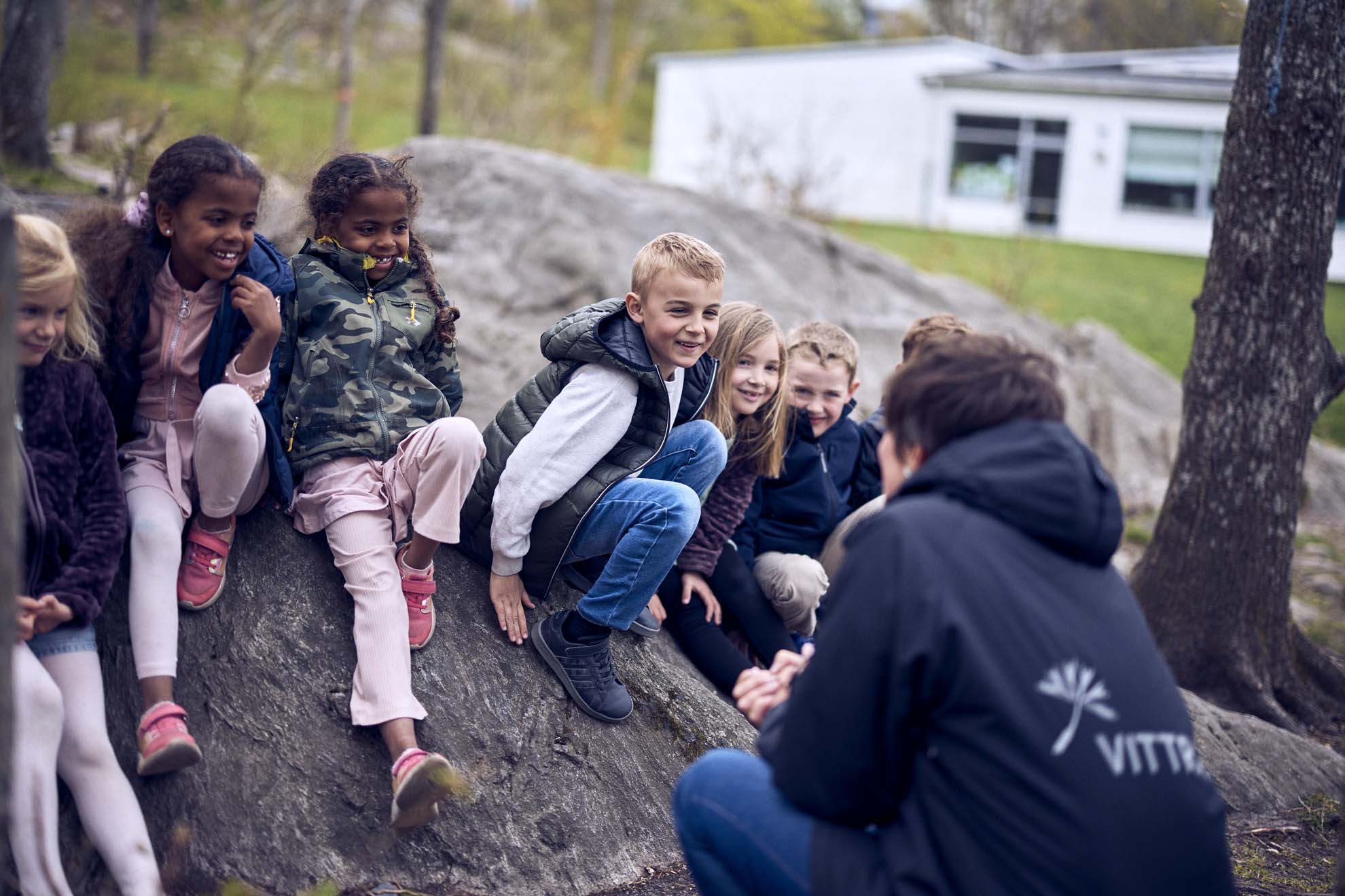 Elever i förskoleklass på Vittra Luma Park sitter utomhus och lyssnar på en lärare.