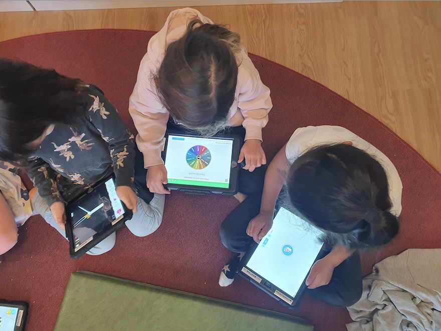 Tre barn sitter med ipads på en soffmodul.