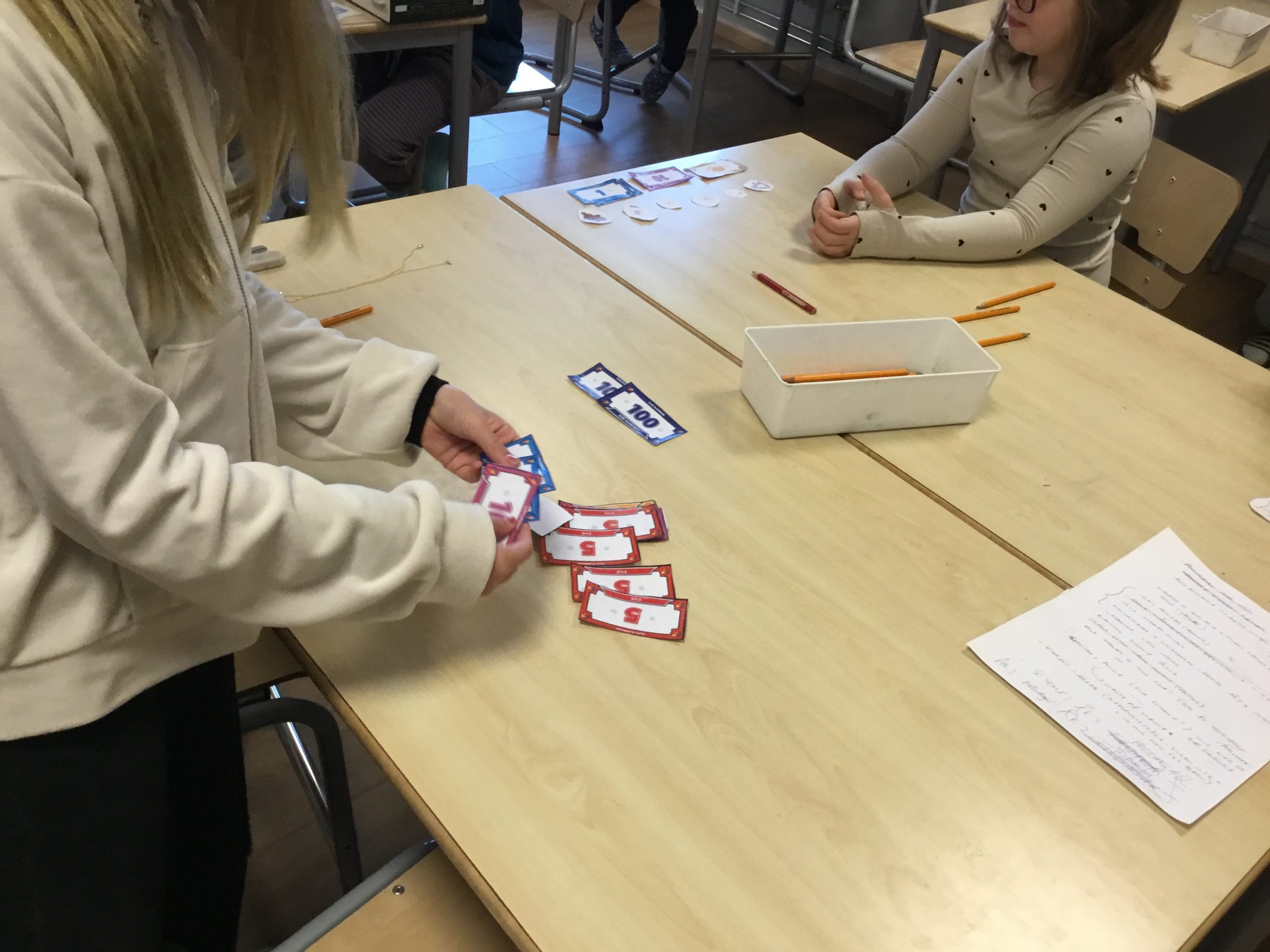 Elever står vid ett bord och leker med låtsassedlar.