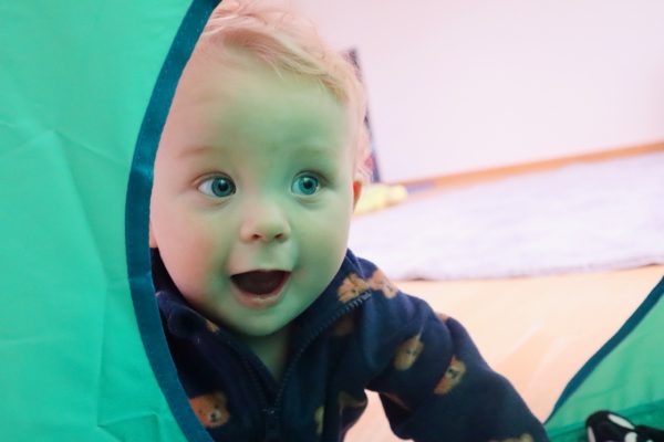 Liten pojke leker på golvet i en grön leksakstunnel.