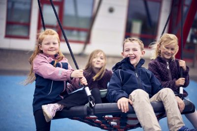 Fyra glada elever på Vittra sitter i en gunga på skolgården.