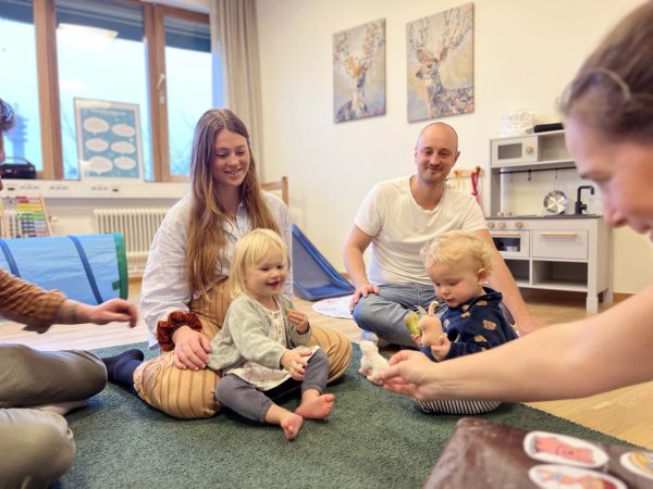 Föräldrar och barn sitter på golvet och leker på öppen förskola.