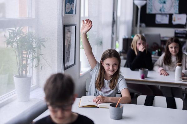 tjej räcker upp handen i klassrummet.