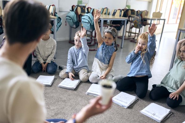 En förskoleklass på Vittra Halmstad sitter i en ring på golvet och lyssnar på läraren.